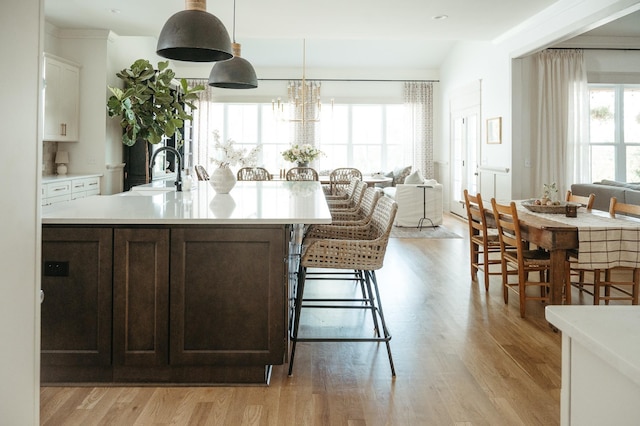 kitchen with sink, white cabinetry, a center island with sink, hanging light fixtures, and light wood-type flooring