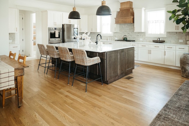 kitchen featuring premium range hood, white cabinetry, stainless steel appliances, and decorative light fixtures