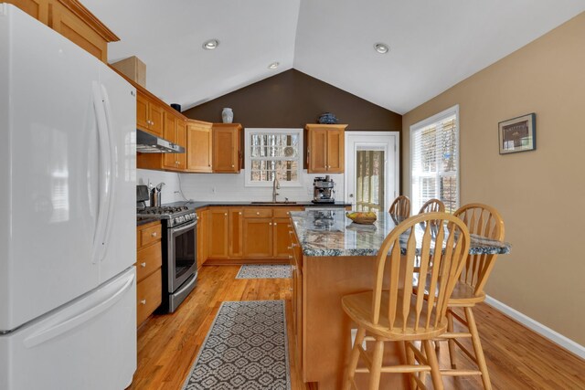 kitchen featuring gas stove, sink, a center island, dark stone counters, and white refrigerator