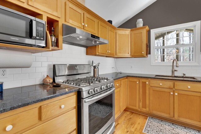 kitchen with appliances with stainless steel finishes, light hardwood / wood-style flooring, dark stone counters, lofted ceiling, and sink