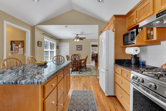 kitchen with dark stone counters, gas range, vaulted ceiling, white refrigerator, and light wood-type flooring