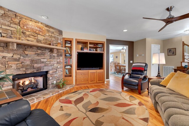 living room featuring ceiling fan, light wood-type flooring, and a stone fireplace