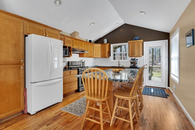 kitchen with a wealth of natural light, a center island, white refrigerator, stainless steel gas range, and a breakfast bar area