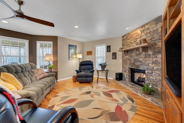 living room featuring ceiling fan, light hardwood / wood-style floors, and a stone fireplace