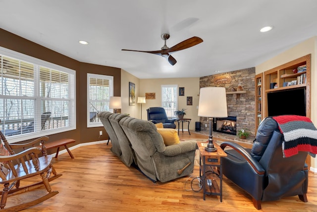 living room with ceiling fan, built in shelves, a stone fireplace, and light hardwood / wood-style flooring