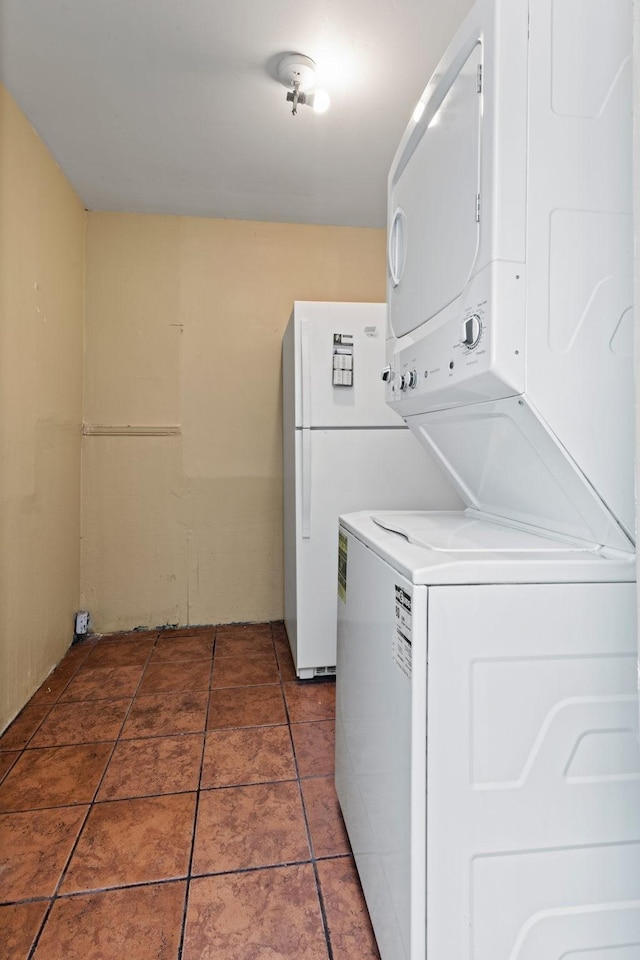 laundry room featuring stacked washer and dryer and dark tile patterned flooring