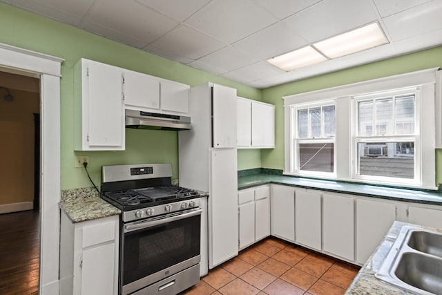 kitchen with light tile patterned flooring, white cabinetry, sink, stainless steel range with gas stovetop, and a drop ceiling