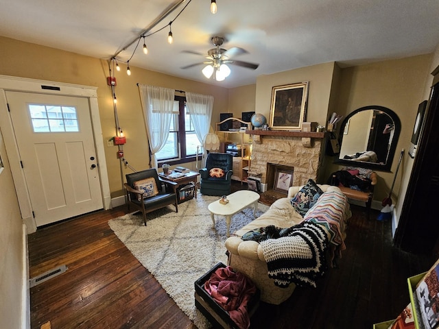 living room featuring dark wood-type flooring, ceiling fan, and a stone fireplace