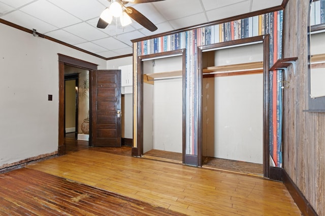 unfurnished bedroom with a drop ceiling, hardwood / wood-style flooring, ornamental molding, and ceiling fan