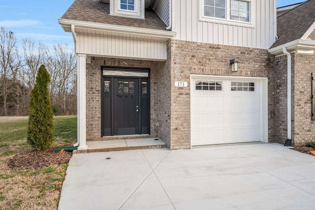 doorway to property featuring brick siding, a shingled roof, an attached garage, board and batten siding, and driveway