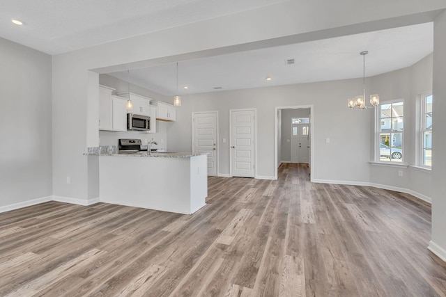 kitchen featuring white cabinets, appliances with stainless steel finishes, decorative light fixtures, a peninsula, and light stone countertops