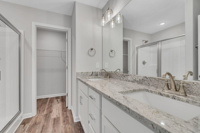 full bathroom featuring a sink, a spacious closet, a shower stall, and wood finished floors