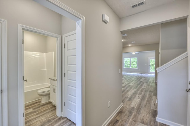 hallway featuring visible vents, baseboards, and wood finished floors