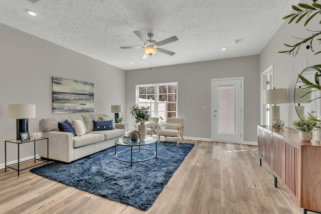 living area featuring a ceiling fan, a textured ceiling, baseboards, and wood finished floors