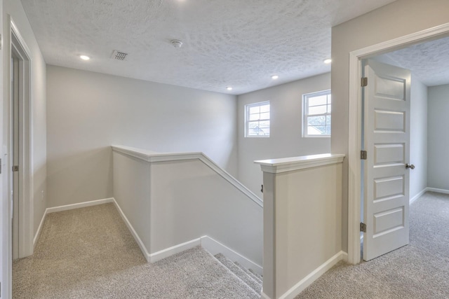 hall with baseboards, light colored carpet, a textured ceiling, an upstairs landing, and recessed lighting