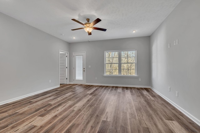 empty room featuring a textured ceiling, wood finished floors, a ceiling fan, and baseboards