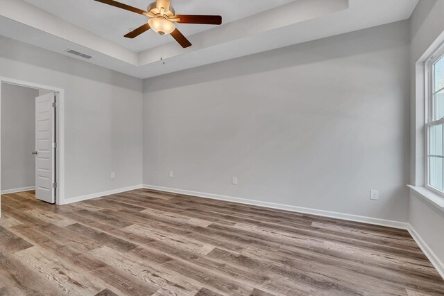 empty room featuring a raised ceiling, wood finished floors, visible vents, and baseboards