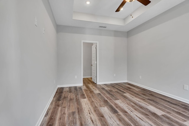 empty room featuring wood finished floors, a ceiling fan, visible vents, baseboards, and a tray ceiling