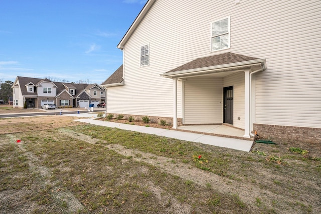 property entrance featuring a residential view, a lawn, a patio, and roof with shingles