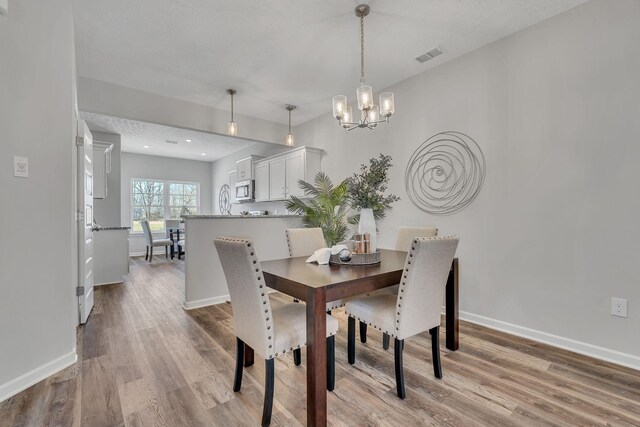 dining space featuring baseboards, an inviting chandelier, visible vents, and light wood-style floors