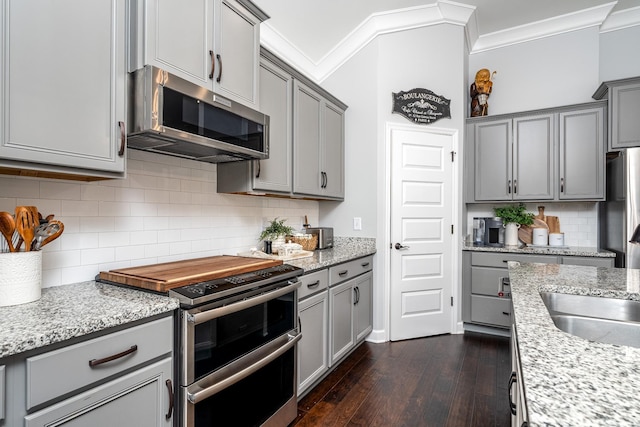 kitchen with appliances with stainless steel finishes, backsplash, light stone counters, ornamental molding, and dark hardwood / wood-style flooring
