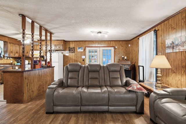 living room featuring dark wood-type flooring, wood walls, a textured ceiling, ornamental molding, and ceiling fan