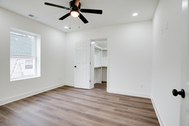 unfurnished bedroom featuring ceiling fan, a walk in closet, and light hardwood / wood-style floors