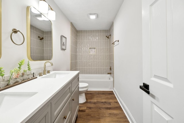 full bathroom featuring toilet, wood finished floors, a sink, double vanity, and washtub / shower combination