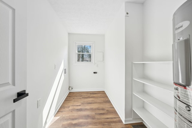laundry area featuring a textured ceiling, laundry area, wood finished floors, baseboards, and water heater