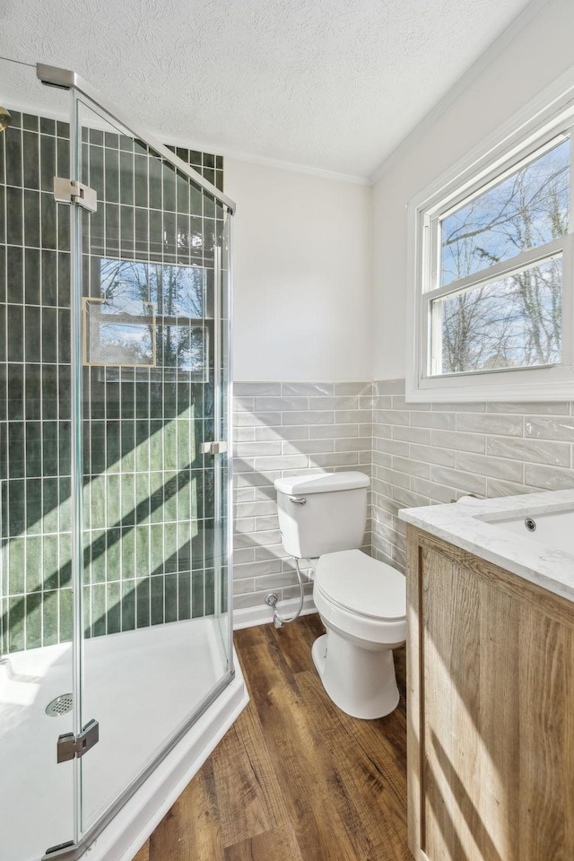 bathroom with tile walls, toilet, a stall shower, a textured ceiling, and wood finished floors