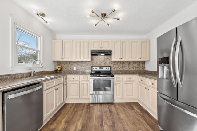 kitchen with appliances with stainless steel finishes, dark countertops, under cabinet range hood, and cream cabinets