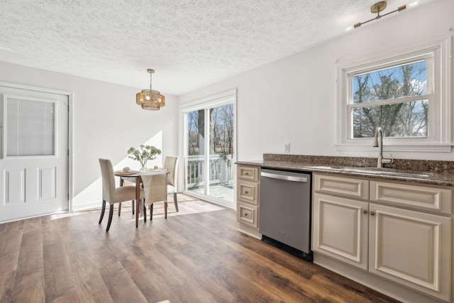 kitchen with dark countertops, dark wood-type flooring, decorative light fixtures, stainless steel dishwasher, and a sink