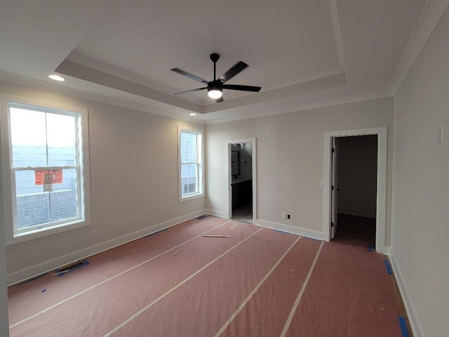 unfurnished bedroom with a raised ceiling, ornamental molding, ceiling fan, and ensuite bath