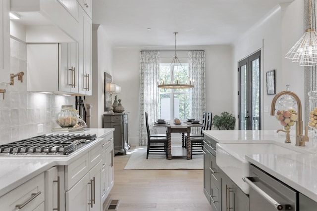 kitchen featuring hanging light fixtures, stainless steel appliances, light stone countertops, light hardwood / wood-style floors, and white cabinets