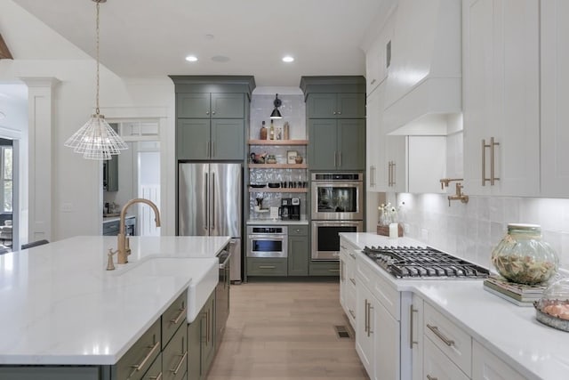 kitchen featuring stainless steel appliances, premium range hood, white cabinets, and decorative light fixtures