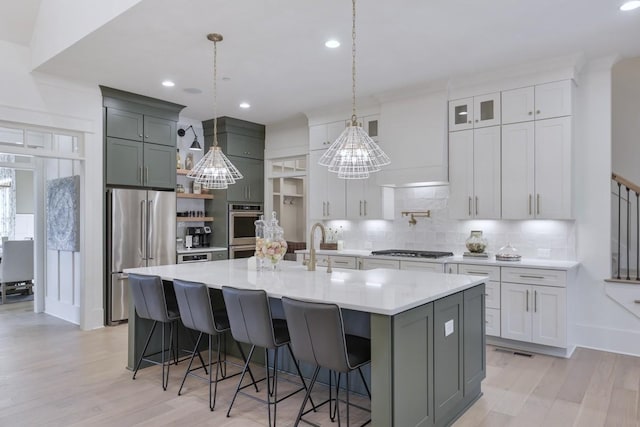 kitchen with appliances with stainless steel finishes, a kitchen island with sink, light hardwood / wood-style floors, decorative backsplash, and decorative light fixtures