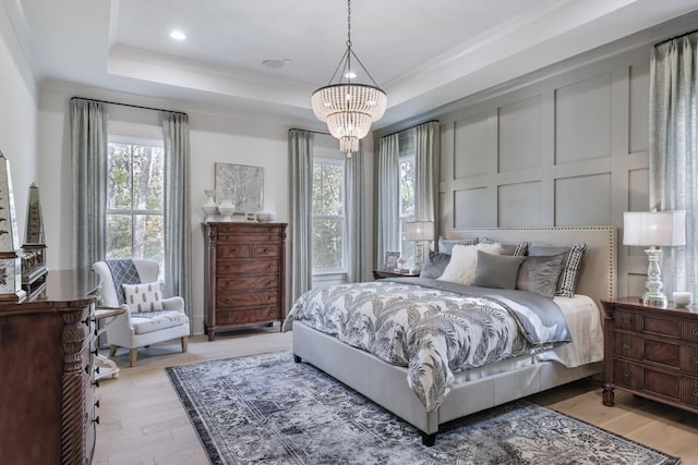 bedroom with a raised ceiling, an inviting chandelier, and light hardwood / wood-style flooring