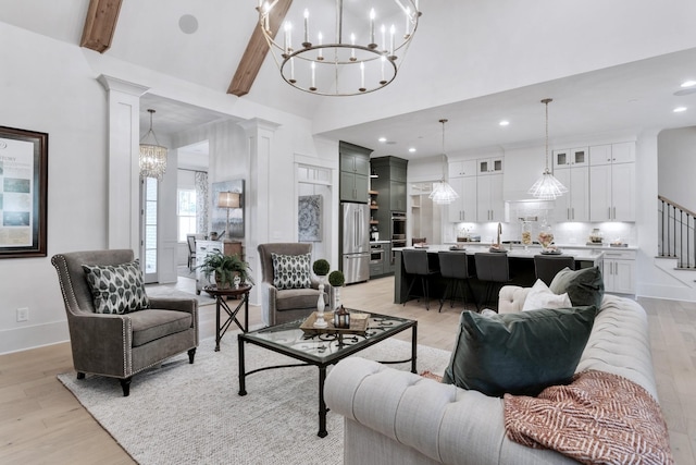 living room featuring ornate columns, a chandelier, a towering ceiling, beam ceiling, and light hardwood / wood-style floors