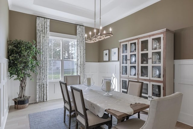 dining space featuring an inviting chandelier, ornamental molding, a raised ceiling, and light wood-type flooring