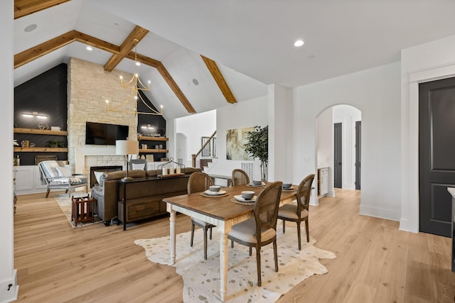 dining room with beamed ceiling, high vaulted ceiling, a fireplace, and light hardwood / wood-style floors