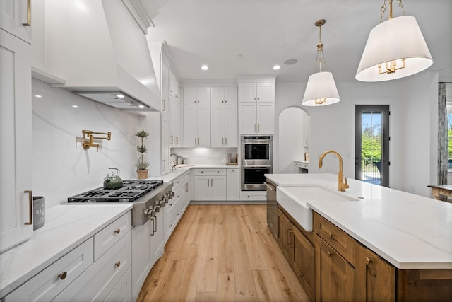 kitchen with sink, white cabinets, a center island with sink, decorative light fixtures, and custom exhaust hood