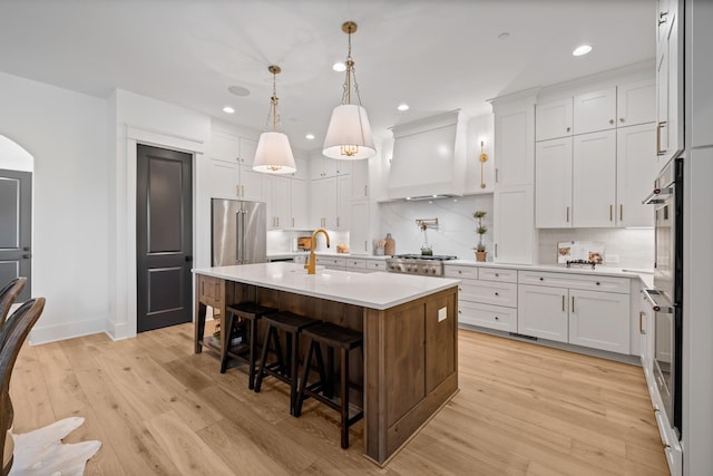 kitchen featuring a breakfast bar, white cabinetry, custom range hood, an island with sink, and decorative light fixtures