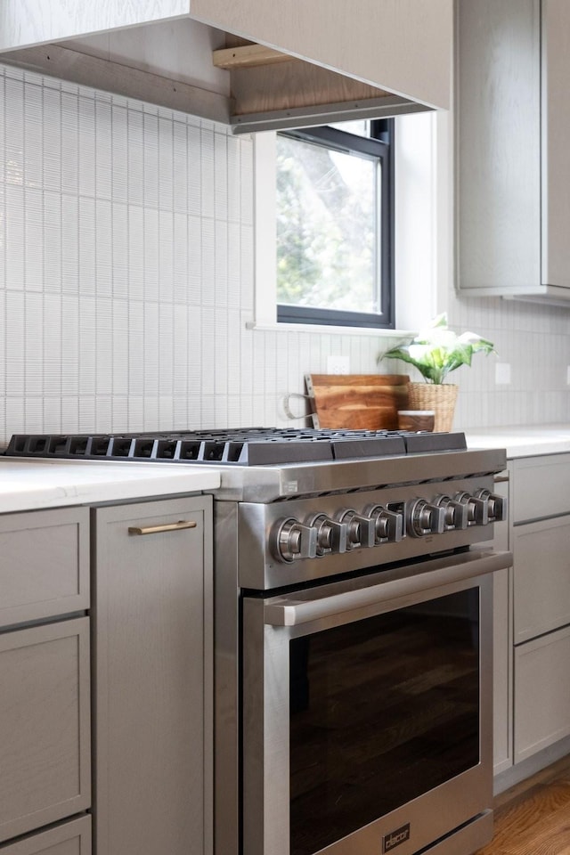 kitchen featuring light wood-style flooring, light countertops, backsplash, gray cabinets, and high end range