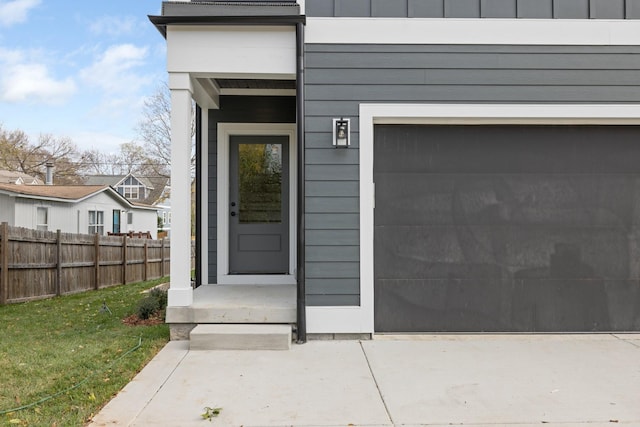 doorway to property featuring board and batten siding, fence, and a garage