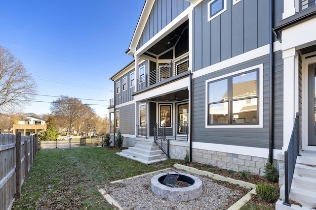 view of side of property featuring board and batten siding, an outdoor fire pit, fence, and a balcony