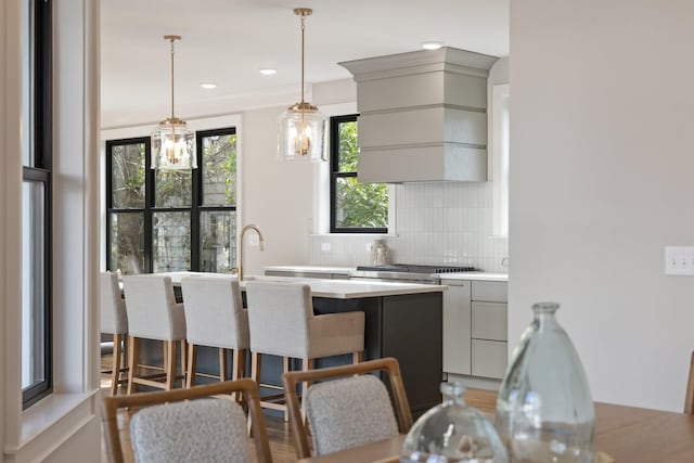 kitchen featuring gray cabinets, light countertops, decorative backsplash, premium range hood, and a kitchen bar