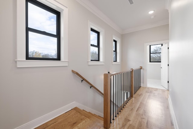 hall with light wood finished floors, ornamental molding, an upstairs landing, and baseboards