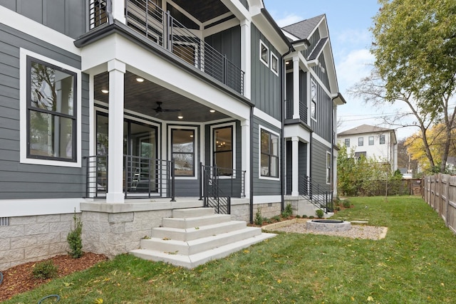 doorway to property with a lawn, a ceiling fan, covered porch, fence, and board and batten siding