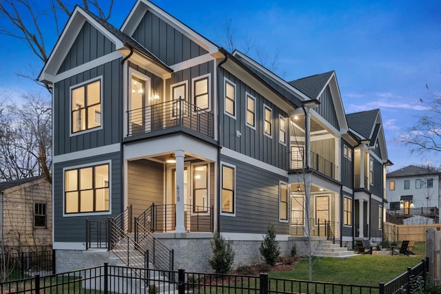 view of front of house featuring a fenced front yard, a balcony, a shingled roof, a front lawn, and board and batten siding