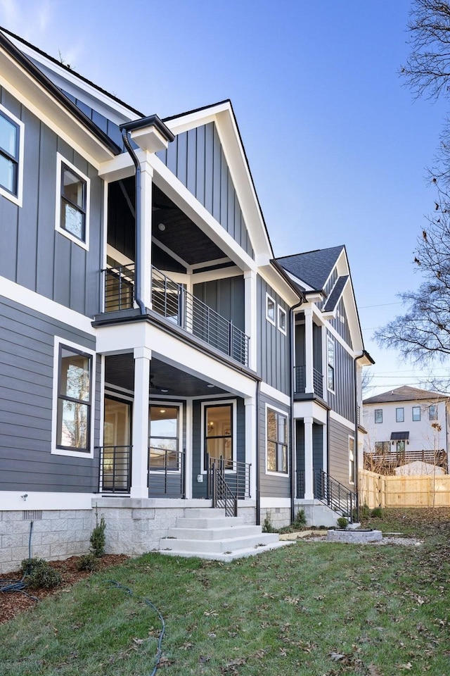 rear view of property featuring board and batten siding, a yard, a balcony, and fence